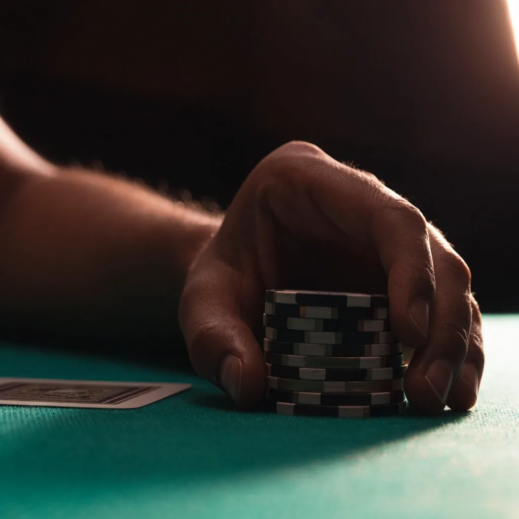 Detail ruky s hromádkou pokerových žetonů nad zeleným suknem stolu