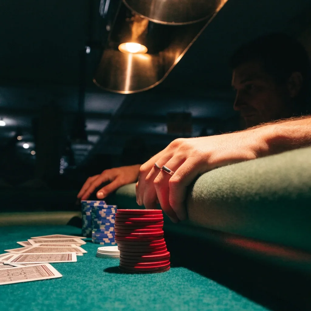 Pokerový stůl v temné herně se sloupci žetonů a rozdanými kartami pod nízkou lampou